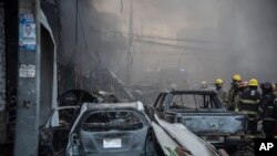 Los bomberos trabajan junto a vehículos destruidos tras una fuerte explosión ocurrida en San Cristóbal, República Dominicana, el 14 de agosto de 2023.