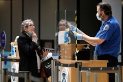A traveler pulls down her protective mask as a TSA agent compares her face to her identification at a security entrance at Seattle-Tacoma International Airport, May 18, 2020, in SeaTac, Wash.