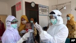 FILE - Health workers in protective gear prepare a measles vaccine to be given to a baby at a community health center in Tangerang, Indonesia, May 12, 2020.