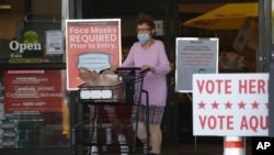 A shopper wearing a mask for protection against COVID-19 leaves a grocery store that is also serving as an early polling site, July 9, 2020, in Austin, Texas.