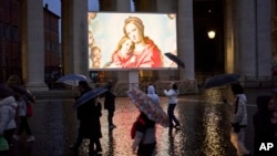 People shelter against the rain as they follow a live broadcast of the Rosary prayer for Pope Francis, in St. Peter's Square at the Vatican, March 12, 2025.