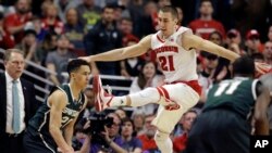 Travis Trice, kiri, berada di bawah Josh Gasser (21) di paruh kedua pertandingan bola basket kampus NCAA di kejuaraan turnamen Big Ten Conference di Chicago, Minggu, 15 Maret 2015. (Foto: AP / Nam Y. Huh )