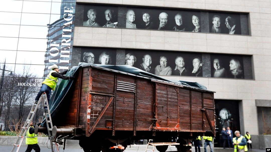 Portraits of Holocaust survivors are displayed at the Museum of Jewish Heritage as a vintage German train car, like those used to transport people to Auschwitz and other death camps, is uncovered on tracks outside the museum, in New York, Sunday, March 31, 2019. 