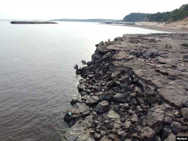 FILE - People are seen in the area where ancient stone carvings on a rocky point of the Amazon River were exposed after water levels dropped to record lows during a drought in Manaus, Amazonas state, Brazil October 23, 2023. (REUTERS/Suamy Beydoun)