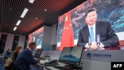 FILE - Journalists sit next to screens showing Chinese President Xi Jinping delivering a speech via video at a media center in Shanghai, Nov. 4, 2020.