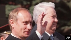 FILE - Russian President Vladimir Putin, left, waves as he stands with former President Boris Yeltsin during a parade on Red Square, in Moscow, May 9, 2000. 