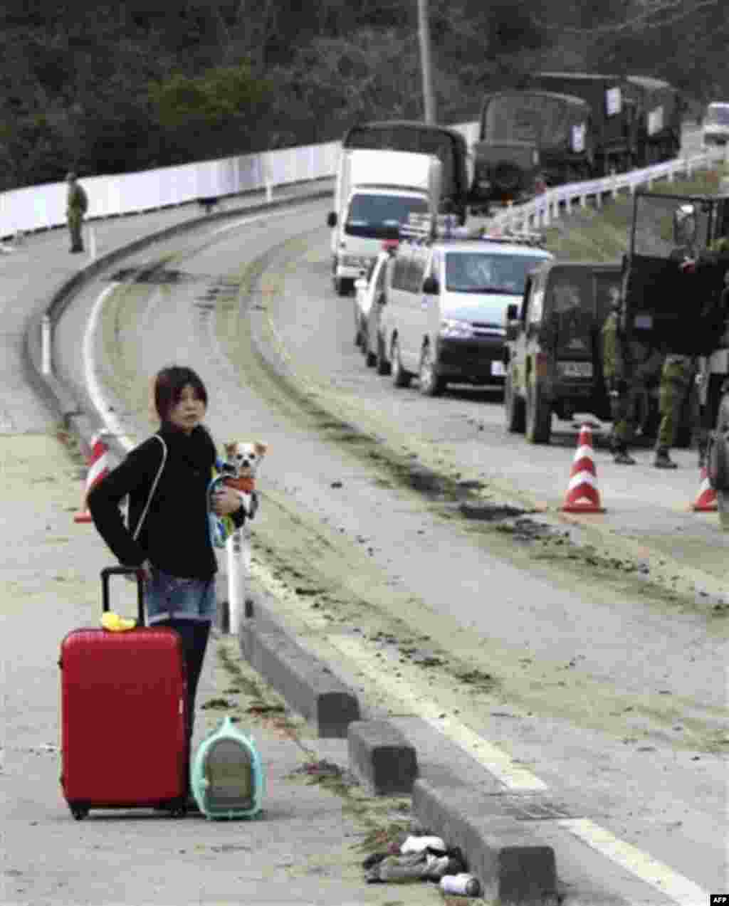 A woman with her pet dog and belongings pauses on the way from her devastated area in Higashimatsushima, Miyagi Prefecture, northern Japan, Monday, March 14, 2011, three days after a powerful earthquake-triggered tsunami hit the country's east coast. (AP 