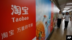 FILE - People walk past an advertising billboard showing the mobile app of Alibaba’s Taobao consumer-to-consumer site at a subway station in Beijing.
