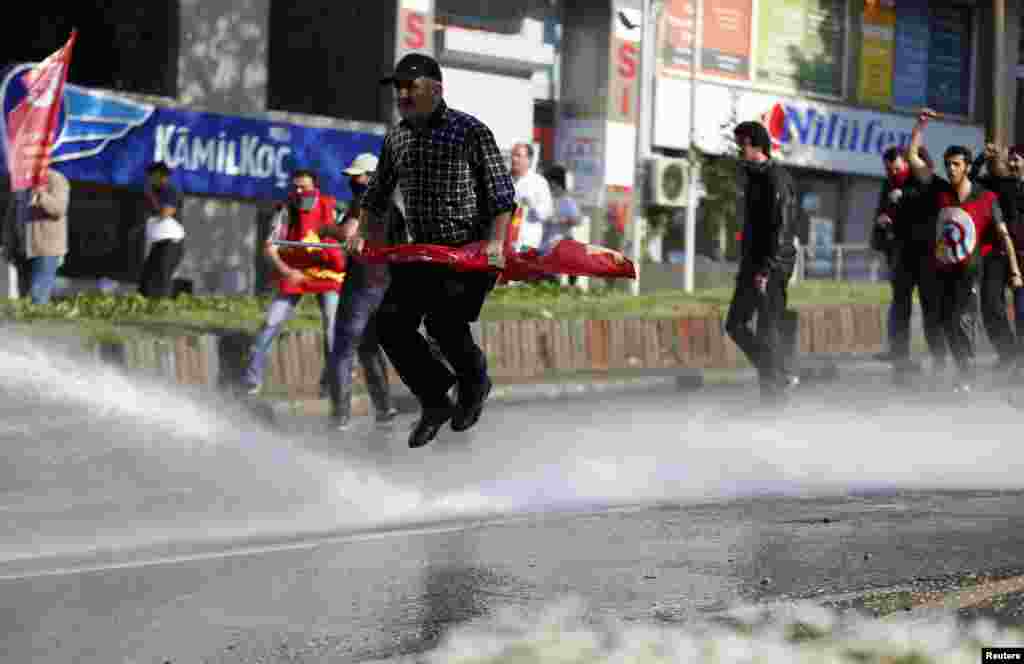 Seorang demonstran Hari Buruh melompat untuk menghindari meriam air di tengah bentrokan antara polisi dan demonstran yang hendak menerobos barikade di Istanbul, Turki (1/5).