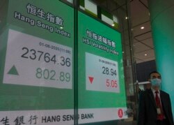 A man wearing a face mask walks past a bank electronic board showing the Hong Kong share index at Hong Kong Stock Exchange, June 1, 2020.