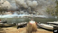 Boats are pulled ashore as smoke and wildfires rage behind Lake Conjola, Australia, Jan. 2, 2020.