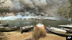 Perahu-perahu diamankan ke pesisir pantai sementera kebakaran lahan membara di Boats are pulled ashore as smoke and wildfires rage behind Lake Conjola, Australia, Jan. 2, 2020.