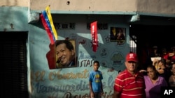 Un grupo se encuentra cerca de un mural con fotografías del difunto presidente de Venezuela Hugo Chávez y del presidente Nicolás Maduro mientras esperan una manifestación en apoyo de Maduro, en el barrio 23 de Enero en Caracas. 13 de julio de 2023. (Foto AP/Ariana Cubillos)