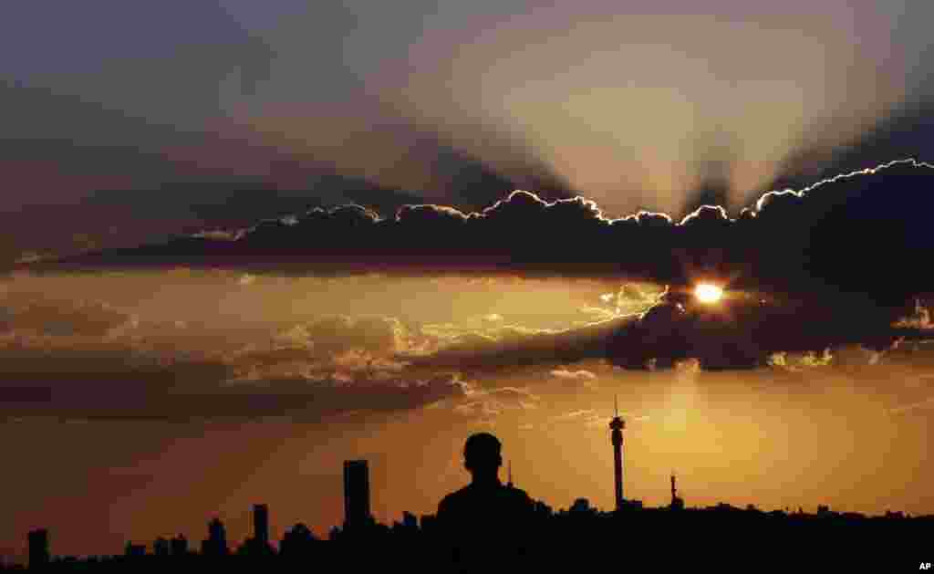 A man watches the sun set against the skyline in Johannesburg, South Africa, March. 10, 2015. 