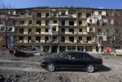 FILE - A man drives a car past a damaged building following shelling in the town of Shushi (Shusha) during fighting over the breakaway region of Nagorno-Karabakh, Oct. 29, 2020.