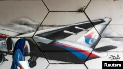 FILE - A woman walks past graffiti of Flight MH370 in Kuala Lumpur.