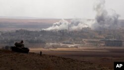 Turkish soldiers in a a tank hold their position on a hilltop on the outskirts of Suruc, at the Turkey-Syria border, overlooking smoke rising from an airstrike by the US-led coalition aircrafts in Kobani, Syria, during fighting between Syrian Kurds and the militants of Islamic State group, Thursday, Oct. 9, 2014. 