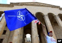 Seorang demonstran oposisi mengibarkan bendera NATO saat unjuk rasa di depan gedung Parlemen Georgia di Tbilisi, Georgia, Sabtu, 6 Juli 2019. (Foto: AP)