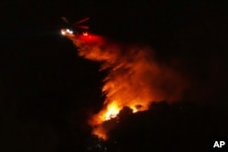 A helicopter drops water on a fire as it burns along Interstate 405, Jan. 23, 2025, in Los Angeles.