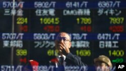 FILE - a man is reflected on an electronic stock indicator of a securities firm in Tokyo. From Australia to Zambia, Chile to Indonesia, the pain of China’s sharp economic slowdown is being felt in the form of depressed commodity prices, elevated unemployment and shrunken home prices, Nov. 4, 2015.