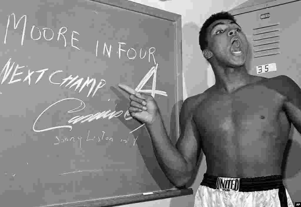 FILE - Young heavyweight boxer Cassius Clay, who later changed his name to Muhammad Ali, points to a sign he wrote on a chalk board in his dressing room before his fight against Archie Moore in Los Angeles, predicting he'd knock Moore out in the fourth ro