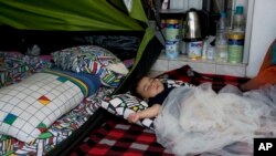 FILE - Yaldof Natzafi, a 1 year -old Afghan baby girl, sleeps at a make shift tent at the west terminal of an abandoned old airport which is used as a shelter for thousands of migrants, in southern Athens, Monday, June 20, 2016. 