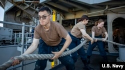 ژمارەیەک سەرباز سەرقاڵی لەنگەرگرتنی کەشتی فڕۆکە هەڵگری ئەبراهام لینکنن لە بنکەیەکی هێزی دەریایی