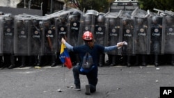 FILE - A man kneels in front of police blocking a march called by opposition leader Juan Guaido, in Caracas, Venezuela, March 10, 2020. 