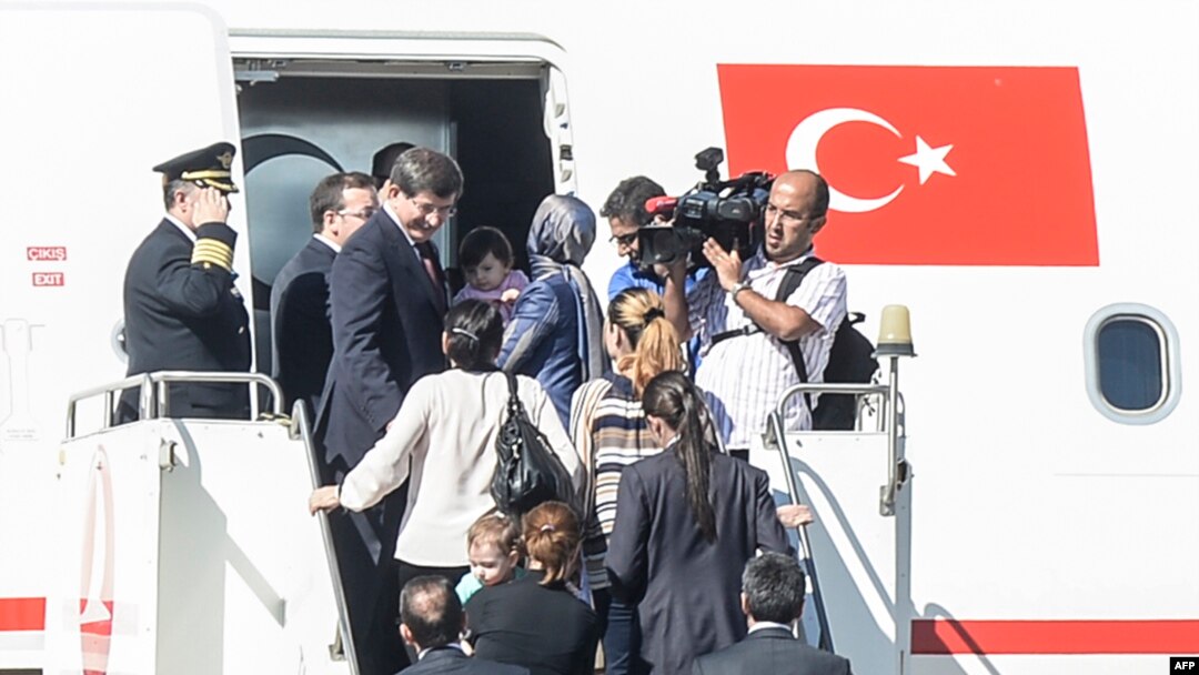 PM Turki Ahmet Davutoglu (kiri) berada di tangga pesawat bersama para sanders yang dibebaskan oleh ISIS di bandara Sanliurfa, selatan Turki dekat perbatasan Suriah (20/9).