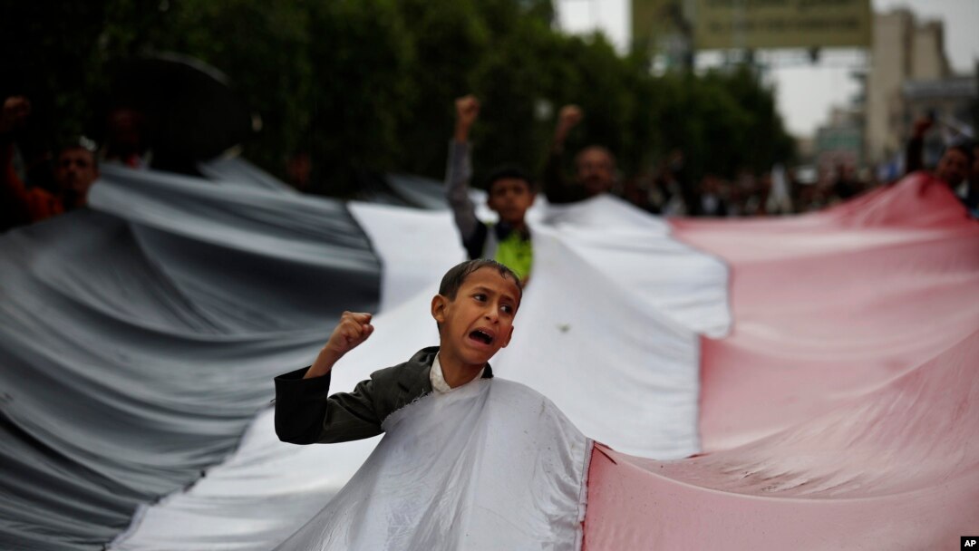 A boy chants slogans through a gap in a national flag raised by Shiite rebels, known as Houthis, during a protest against Saudi-led airstrikes in Sanaa, Yemen, April 15, 2016. 