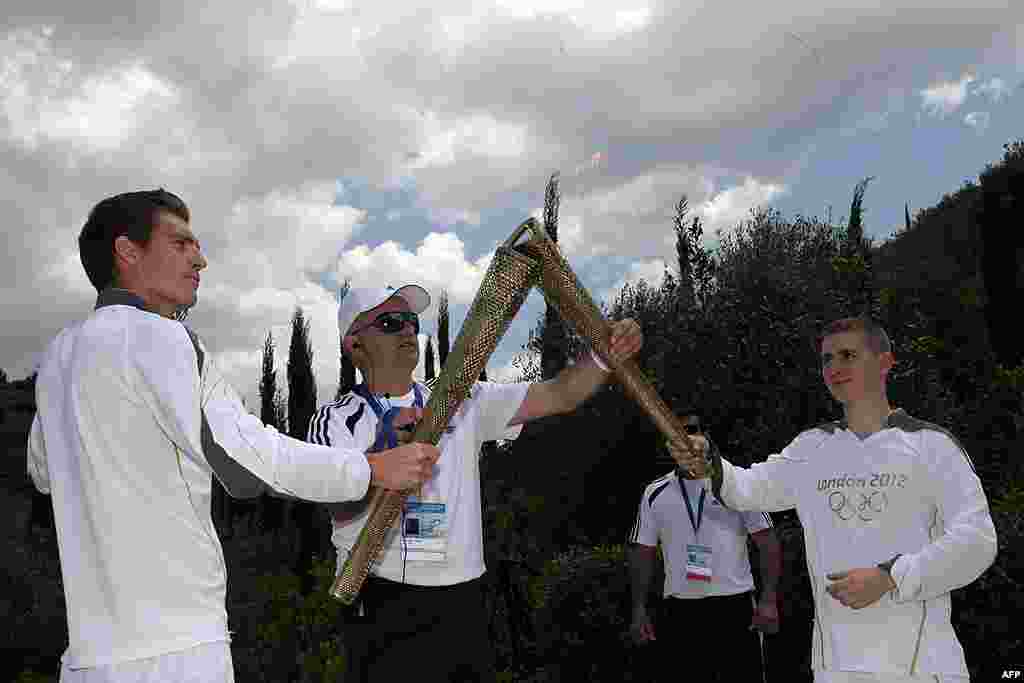 Second Olympic Torch bearer, Alex Loukos from Great Britain, right, receives the Olympic torch from Spyros Gianniotis, left. (AP)