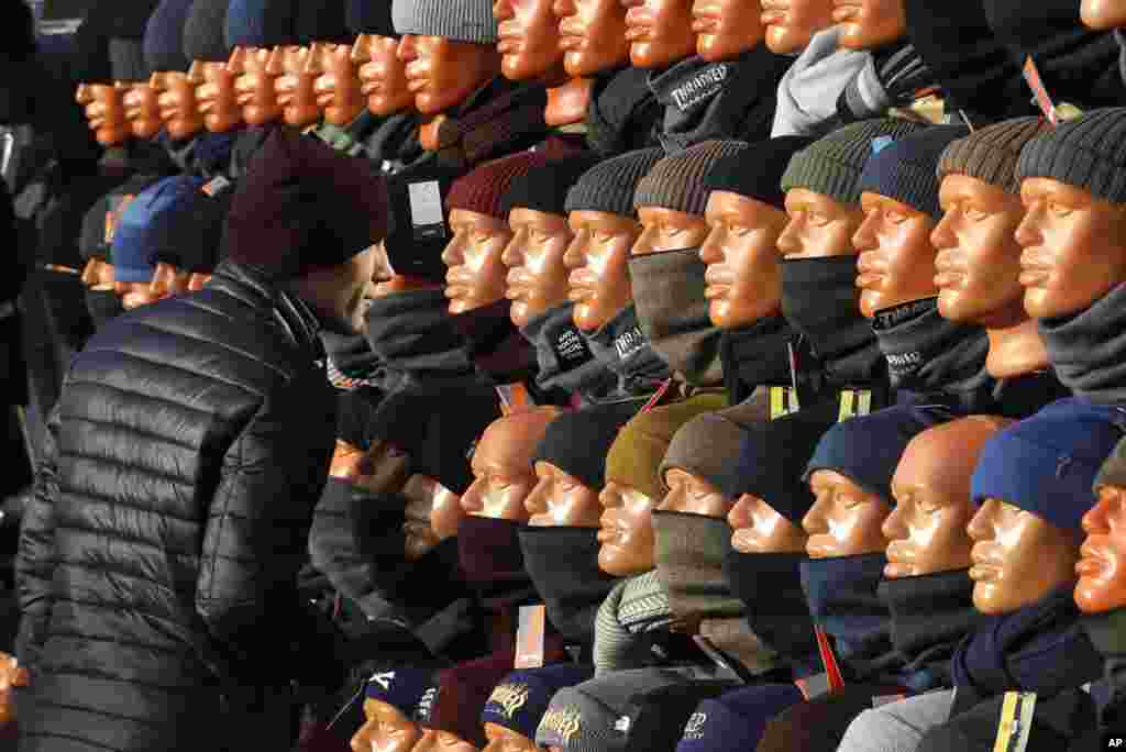 A man looks at himself in a mirror, hidden between mannequins, as he chooses a cap at the clothing market in Minsk, Belarus.