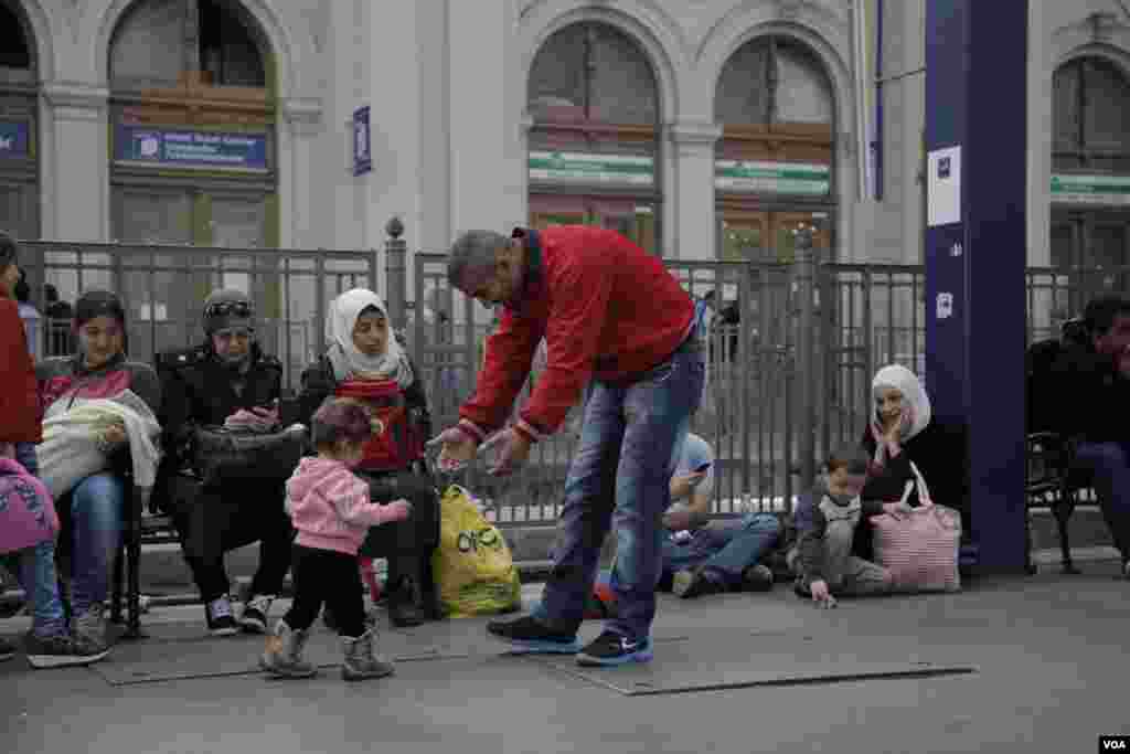 پدری سوری در انتظار قطار بر روی سکوی ایستگاه به کودک خردسالاش راه رفتن یاد میدهد