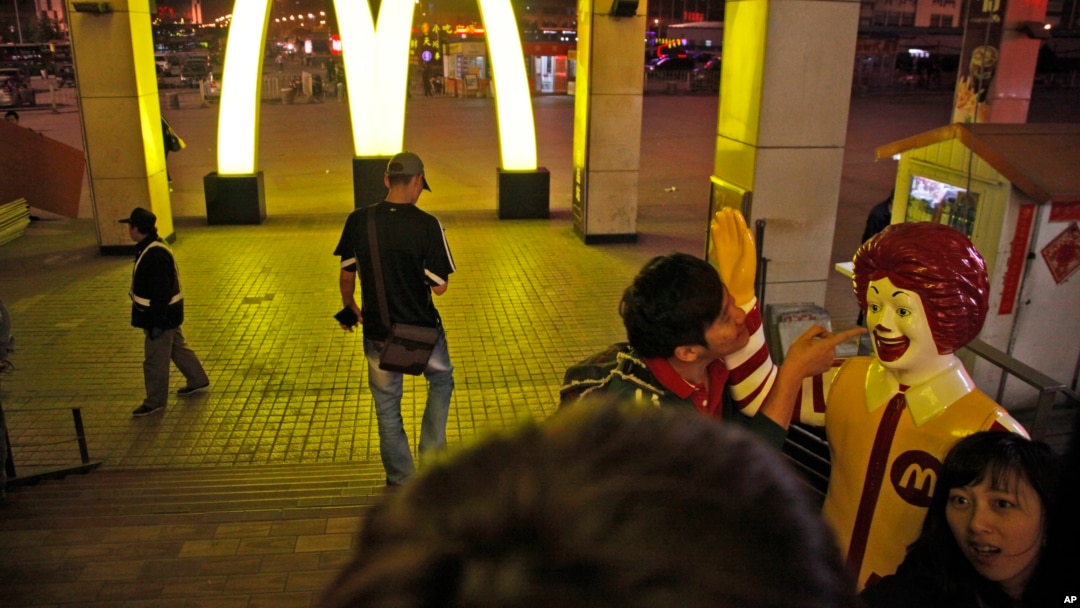 FILE - A Chinese man poses for photos with Ronald McDonald, the mascot for fast food restaurant McDonald's, outside one of its branch at a train station in Shenyang in northern China's Liaoning province. 