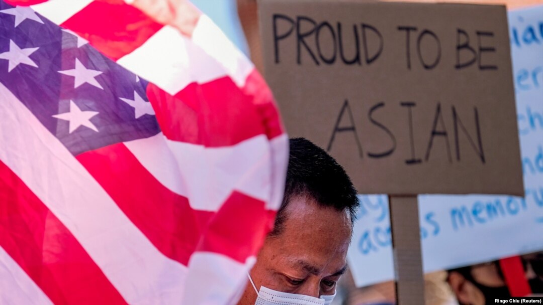 Seorang demonstran berdiri di antara bendera AS dan sebuah poster saat unjuk rasa menentang kejahatan kebencian terhdapa warga Asia-Amerika di luar balai kota Los Angeles, California, Sabtu, 27 Maret 2021. (Foto: Ringo Chiu/Reuters)