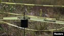 A cross stands among police tape set up to mark a mass grave found next to a cemetery in Tetelcingo, Mexico, Nov. 12, 2015.