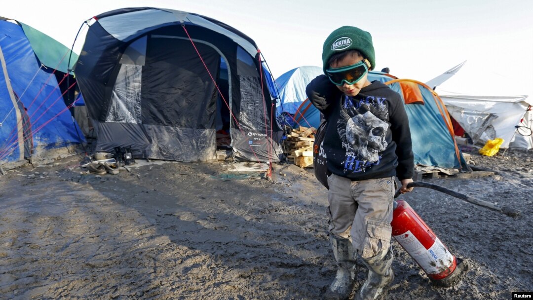 Seorang anak migran menyeret alat pemadam kebakaran di lapangan berlumpur lokasi kamp sementara untuk para migran dan pencari suaka dari Irak, Kurdistan, Iran dan Suriah, di dekat Dunkirk, Perancis, 25 Januari 2016. 