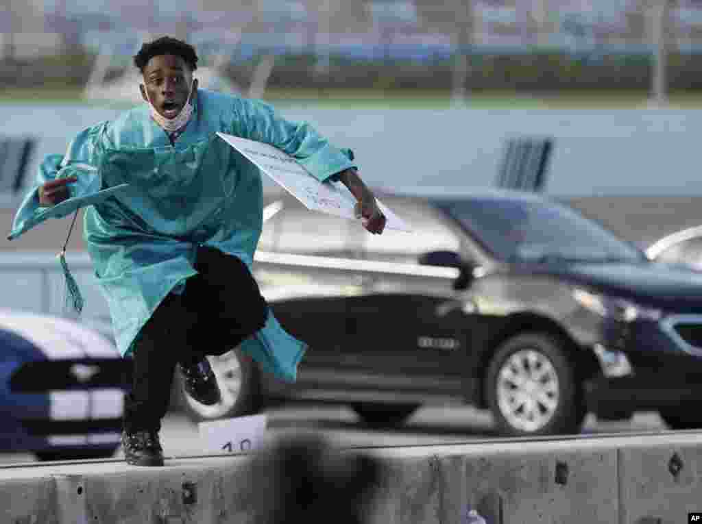 Richardson Fremond leaps over a wall as he runs to collect an award during a graduation ceremony for the senior class of Chambers High School at Homestead-Miami Speedway, in Homestead, Fla., June 23, 2020.