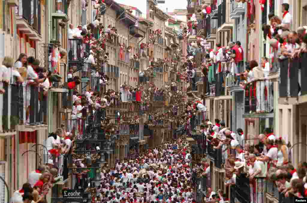 People watch from balconies as revelers sprint in front of bulls and steers during the first running of the bulls at the San Fermin festival in Pamplona, Spain.
