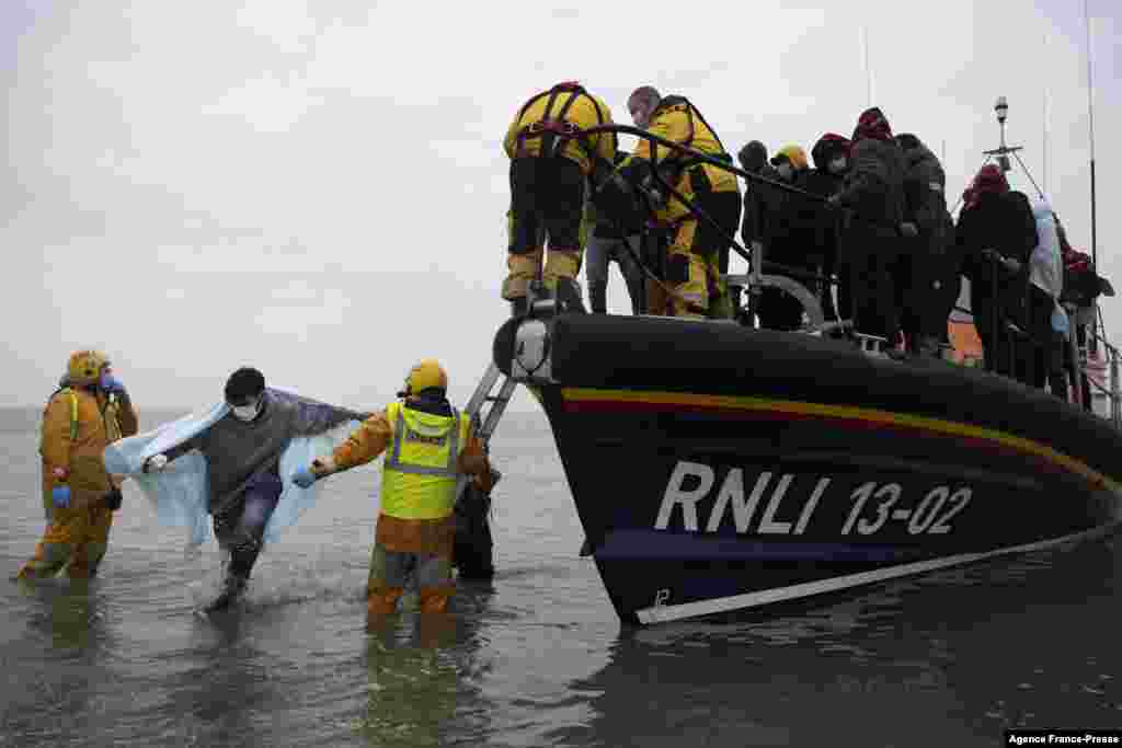 Para migran dibantu menuju ke darat dari kapal RNLI (Royal National Lifeboat Institution) di sebuah pantai di Dungeness, di pantai tenggara Inggris, setelah diselamatkan saat ketika melintasi Selat Inggris (24/11). (Foto: AFP)