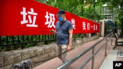 A man wearing a face mask to protect against the spread of the new coronavirus walks past a propaganda banner encouraging people to sort their garbage in Beijing, June 24, 2020.