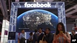 FILE - Visitors pass by the booth for social media giant Facebook at the China International Import Expo in Shanghai, Nov. 6, 2019.