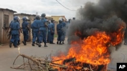 Burundian riot police march past a burning tyre roadblock following clashes with opposition protesters in a street in the capital Bujumbura, April 26, 2015.