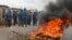Burundian riot police march past a burning tyre roadblock following clashes with opposition protesters in a street in the capital Bujumbura, April 26, 2015.