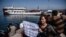 A woman activist holds a placard as a small Turkish ferry carrying migrants who are deported to Turkey arrives on April 4, 2016 at the port of Dikili district in Izmir.
