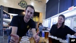 Koby Harris, brewery production manager, left, and Sandra Cain, assistant director of retail operations, present freshly brewed beers at Innovation Brew Works, California State Polytechnic University in Pomona, Calif., March 19, 2015.