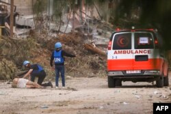 FILE - UN staff approach a wounded Palesinian reportedly shot by Israeli forces while leaving Gaza City through the Zeitoun district on its southern entrance to carry him into an ambulance on November 25, 2023.