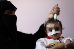 FILE - A woman uses a syringe to feed her malnourished daughter at a malnutrition treatment ward of al-Sabeen hospital in Sana'a, Yemen, Oct. 27, 2020.
