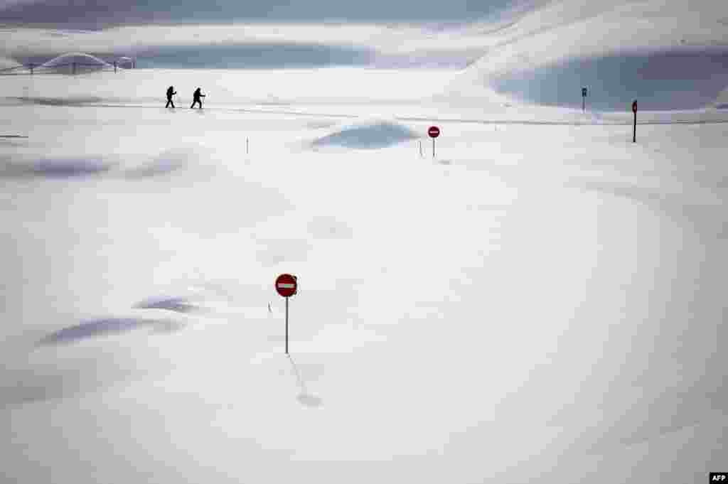 Two skiers pass by traffic signs showing above the snow at the Dappes Car Park near La Dole, Switzerland, Jan. 26, 2021.