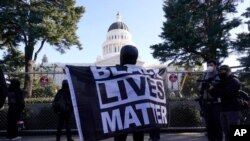 Un manifestante se cubre con una bandera del movimiento Black Lives Matter durante una protesta frente al Capitolio estatal en Sacramento, California, el 20 de enero de 2021.